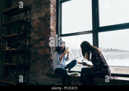 Fröhlicher junger Frauen beim Abendessen sass auf dem Fensterbrett zu Hause Stockfoto