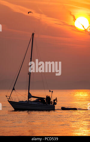 Yacht segeln auf einem ruhigen See bei Sonnenaufgang aus Penmon Punkt, Anglesey, Nordwales Stockfoto