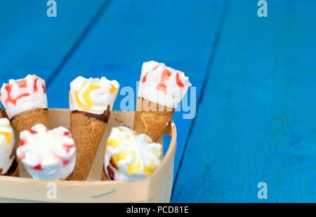 Süße frische Nachtisch, Kälte und Eis Konzept: eine Holzkiste mit Eistüten auf blauem Hintergrund. Stockfoto