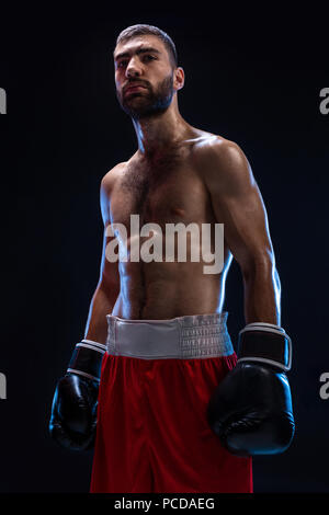 Stattliche athletischer Kerl in einem rote Shorts auf schwarzem Hintergrund. Der Boxer ist das Abrufen von seinem Atem nach dem Üben Haken und bläst. Professionelle Kämpfer. Stockfoto