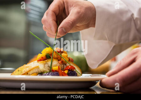Eine Nahaufnahme von den Händen der Koch die letzten Dressing auf einer Platte mit Fisch in einem kommerziellen Küche, Stockfoto
