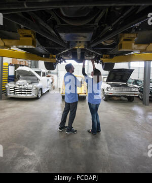 Männliche und weibliche Mechanik arbeiten an der Unterseite des Autos in einer Werkstatt. Stockfoto