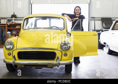 Einem kaukasischen Frauen steht neben Ihr altes Auto in einem klassischen Autowerkstatt. Stockfoto
