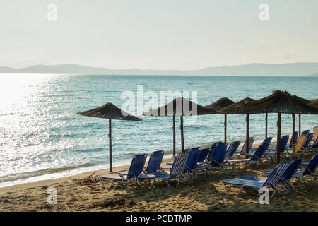 Morgen am Strand mit Liegestühlen unter Palmenblättern Sonnenschirme. In Komotini, Griechenland. Stockfoto