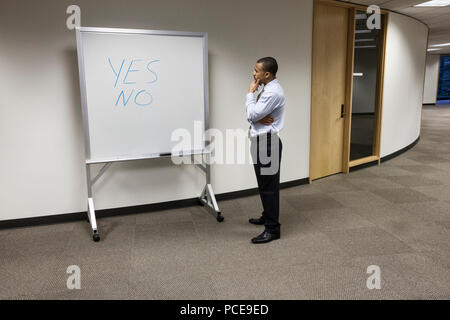 Ein schwarzer Geschäftsmann denken und stand vor einem Büro weiße Tafel mit den Worten "Ja" und "Nein" darauf geschrieben. Stockfoto