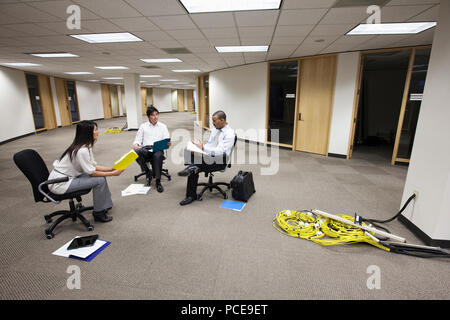 Ein gemischtes Rennen Gruppe von drei Personen sitzen in einem offenen Raum und machen Pläne für das neue Büro Layout. Stockfoto