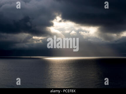 Sonne bricht durch schwarze Gewitterwolken über Meer Stockfoto