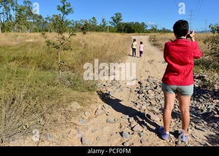 Eine Mutter nimmt ein Foto von Kindern auf eine trockene staubige unfruchtbar Road, Townsville, Queensland, Australien Stockfoto