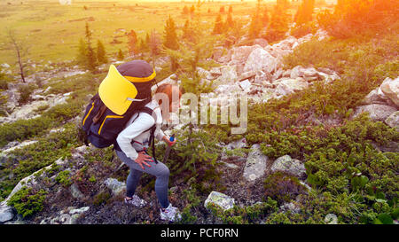 Atmosphärische Moment in die Berge. Wandern Frau mit Rucksack Reisenden auf die Berge. Stilvolle Frau wandern, im Hintergrund ein grüner Wald, fiel Stockfoto