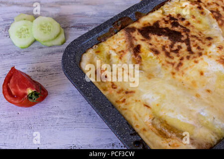 Italienisches Essen. Heiß serviert leckere frisch gebackene Lasagne mit Tomaten und Gurken auf Holztisch. Close-up, Selektive konzentrieren. Stockfoto