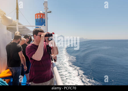 SYMI, Griechenland - 15. Mai 2018: ein Tourist sieht durch das Fernglas auf das Meer von einem Kreuzfahrtschiff. Mittelmeer. Griechenland Stockfoto