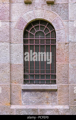 Gewölbte Kirche Fenster mit einer rostigen Gitter und einem Raster gegen eine Mauer aus Stein. Stockfoto