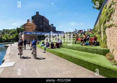 Bei steigenden Temperaturen kühlen sich Sonnenanbeter auf den Stufen am Kanal am Granary Square, King's Cross, London, Großbritannien ab Stockfoto