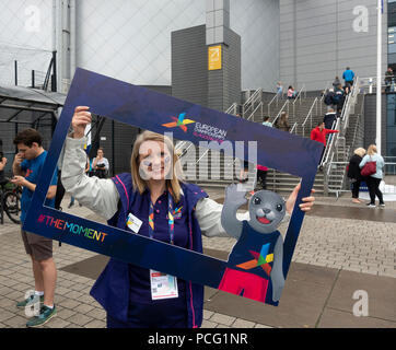 Glasgow, Schottland, Großbritannien. 02 August, 2018. Ein lächelndes Freiwillige posieren für ein Sealfie in einem Frame mit der Spiele Maskottchen Bonnie die Dichtung, außerhalb der Sir Chris Hoy Velodrome (Emirates Arena) in der Gegend von Glasgow Dalmarnock vor der ersten Veranstaltungen der Glasgow 2018, a multi-Sport Events. Die meisten Sportarten wird bewirtet, in Schottland, mit dem Velodrom Hosting die Spur Radsport. Credit: Elizabeth Leyden/Alamy leben Nachrichten Stockfoto