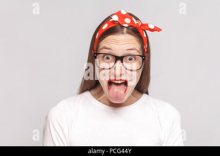 Zunge aus überrascht, schockiert oder verrückt emotionale junge Frau im weißen T-Shirt mit Sommersprossen, schwarze Brille, rote Lippen und Kopfband. indoor Studio s Stockfoto