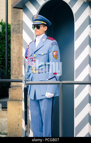 Ein junger Mann in der Sonnenbrille, Sommer Uniform und Mütze steht außerhalb der Prager Burg Tore und gestreifte Schaltschrank auf Pflicht als Teil der Schutzeinrichtung. Der Tschechischen Republik. Stockfoto