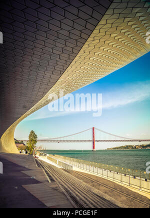Lissabon. Neuer Flügel des MAAT-Museums beim Targus. Berühmte Brücke Ponte 25 de Abril im Hintergrund. Sie erstreckt sich über 2277,64 m über den Fluss Targus. Stockfoto