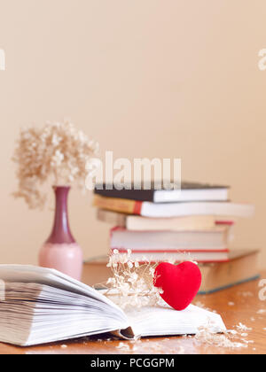 Nahaufnahme des offenes Buch mit Verwelkte Blüten Hortensie und ein kleines rotes Herz, Stapel Bücher auf dem Hintergrund auf Holztisch, Weichzeichner unscharf, copysp Stockfoto