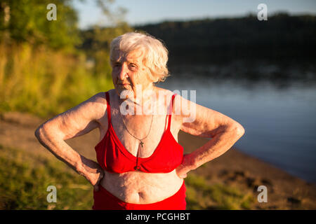 Ältere Frau in einem Badeanzug ist am Ufer des Flusses. Stockfoto