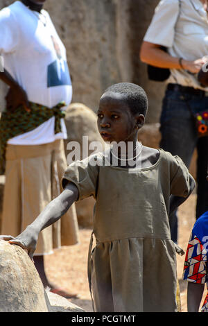 TAMBERMA VIL, TOGO - Jan 13, 2017: Unbekannter Tammari ein kleines Mädchen in einem grauen Kleid ihre Hand auf einen Stein in das Dorf legt. Tammaris sind ethnische gro Stockfoto