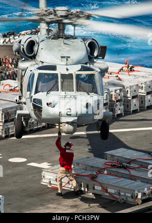 Pazifik (April 28, 2013) ein Crewmitglied an Bord der Military Sealift Command Dry Cargo Munition ship USNS Richard E. Byrd (T-AKE 4) misst der Ladung zu einem MH-60S Sea Hawk Hubschrauber zu den Indianern Hubschrauber Meer Combat Squadron (HSC) 6 zugewiesen, während die Durchführung einer Auffüllung-auf-See mit dem Flugzeugträger USS Nimitz (CVN 68). Der Nimitz und Carrier Air Wing 11 San Diego für einen westlichen Pazifik Bereitstellung links. Stockfoto