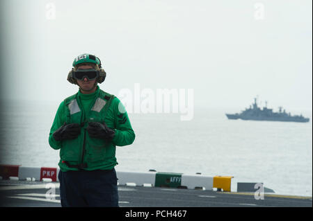 Ein US-Sailor zugeordnet Amphibisches Schiff USS America (LHA 6) wartet auf dem Flugdeck wie der chilenischen Marine Fregatte CNS Capitan Prat (FFGM 11), Hintergrund, Segel, in der Nähe bei einem bilateralen Übung 12.08.27, 2014, im Pazifischen Ozean. Das Amerika, das schiffte sich auf einer Mission Training mit Partner Nationen in Amerika durchzuführen, bevor die Berichterstattung zu seinem neuen Haus Hafen von San Diego. Das Schiff wurde feierlich Okt. 11, 2014 in Betrieb genommen werden. Stockfoto