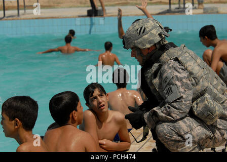 Ein US-Soldat für die persönliche Sicherheit Loslösung, 4 Battalion, 64th Panzer Regiment, 3 Infanterie Division zugeordnet, spricht mit irakischen Jungen, als er bei der Eröffnung eines neuen Schwimmbad in Risalah, Bagdad, Irak, Sept. 18, 2008. Stockfoto