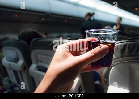 Eine männliche Hand mit einem transparenten Kunststoff Glas mit einem kalten Getränk an Bord der Economy-Klasse eine deutsche Fluggesellschaft, Ansicht von oben. Stockfoto