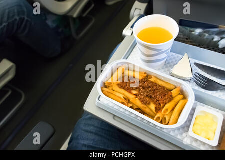 Ein im Flug essen - Mittagessen mit Orangensaft und Pasta an Bord der Economy Klasse einer deutschen Fluggesellschaft. Ansicht von oben. Stockfoto