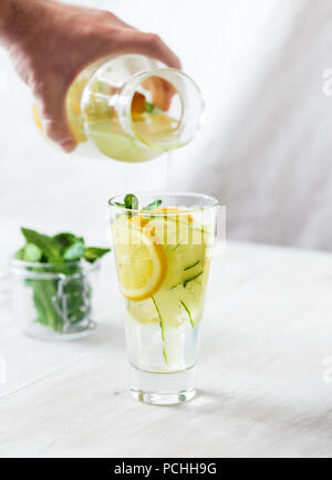 Man gießt in Glas detox Wasser mit Gurke, Zitrone und Minze Stockfoto