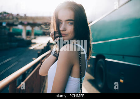 Glückliche junge Frau tragen weiße oben stehend im Freien in der Nähe von Big-Bus auf der Straße am sonnigen Sommertag. Mädchen Reisenden mit langen braunen Haaren und blauen Augen looki Stockfoto