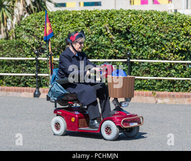 Ältere Dame Reiten in einem Mobility Scooter entlang der Strandpromenade an einem heißen Tag im Sommer in Worthing, West Sussex, England, UK. Stockfoto