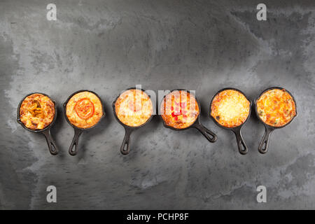 Sechs einzelnen Mini Quiche Torten in Gusseisen Pfannen auf dunklem Schiefer Oberfläche Stockfoto