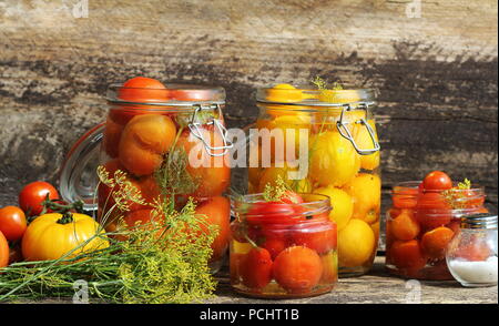 Eingelegte Tomaten in Töpfen auf hölzernen Tisch. Tomaten fermentiert Prozess Gläsern Vielfalt - rot, gelb, orange Stockfoto