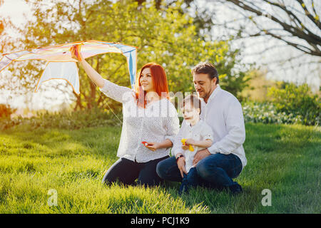 Schöne und stilvolle rothaarige Mama in eine weiße Bluse sitzt im Gras mit ihren schönen Mann in einem weißen Hemd und Jeans gekleidet; sie spielen mit t Stockfoto