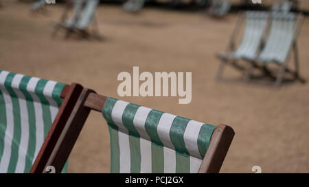 Liegestühle mit grünen und weißen Streifen auf totem Gras in einem ausgetrockneten Hyde Park, London während der Hitzewelle, Juli 2018. Stockfoto