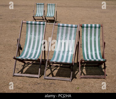Liegestühle mit grünen und weißen Streifen auf totem Gras in einem ausgetrockneten Hyde Park, London während der Hitzewelle, Juli 2018. Stockfoto