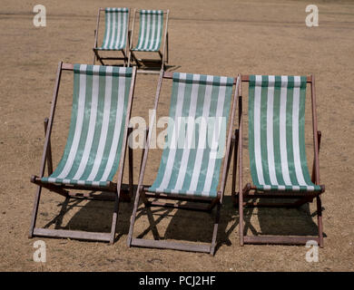 Liegestühle mit grünen und weißen Streifen auf totem Gras in einem ausgetrockneten Hyde Park, London während der Hitzewelle, Juli 2018. Stockfoto