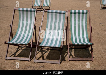 Liegestühle mit grünen und weißen Streifen auf totem Gras in einem ausgetrockneten Hyde Park, London während der Hitzewelle, Juli 2018. Stockfoto
