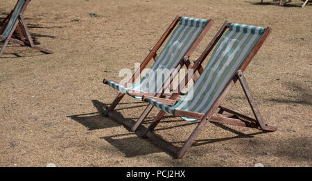 Liegestühle mit grünen und weißen Streifen auf totem Gras in einem ausgetrockneten Hyde Park, London während der Hitzewelle, Juli 2018. Stockfoto