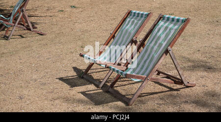 Liegestühle mit grünen und weißen Streifen auf totem Gras in einem ausgetrockneten Hyde Park, London während der Hitzewelle, Juli 2018. Stockfoto