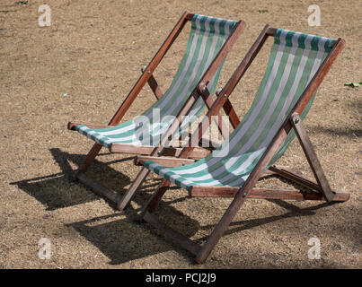 Liegestühle mit grünen und weißen Streifen auf totem Gras in einem ausgetrockneten Hyde Park, London während der Hitzewelle, Juli 2018. Stockfoto