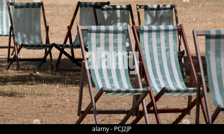 Liegestühle mit grünen und weißen Streifen auf totem Gras in einem ausgetrockneten Hyde Park, London während der Hitzewelle, Juli 2018. Stockfoto