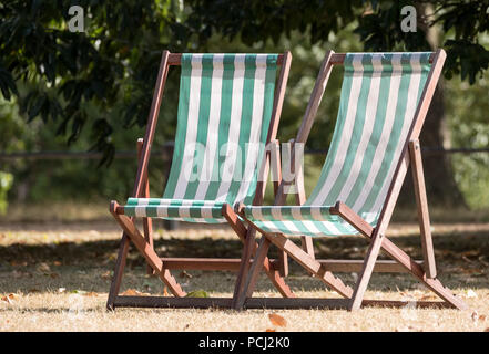Liegestühle mit grünen und weißen Streifen auf totem Gras in einem ausgetrockneten Hyde Park, London während der Hitzewelle, Juli 2018. Stockfoto