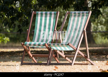 Liegestühle mit grünen und weißen Streifen auf totem Gras in einem ausgetrockneten Hyde Park, London während der Hitzewelle, Juli 2018. Stockfoto