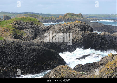 Wellen brechen auf schwarzem Basaltgestein. Ballintoy, Antrim, Nordirland. Stockfoto