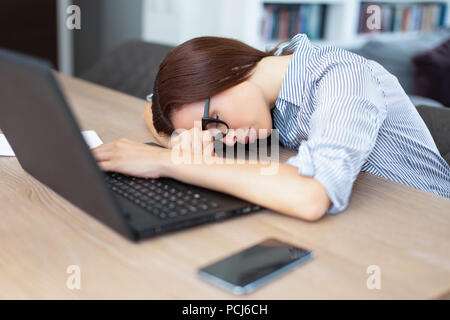 Müde junge brünette Frau schlafen vor Laptop zuhause Stockfoto