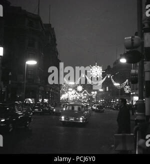 1960, historische, London, Nacht, und Autos der Ära reisen entlang der Regent Street erleuchtet von der traditionellen Weihnachtsbeleuchtung. Stockfoto