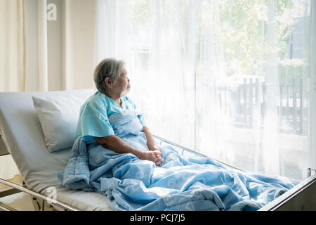 Asiatische gedrückt ältere Frau Patienten liegend auf Bett Blick aus dem Fenster im Krankenhaus. Ältere Frau Patienten ist froh, von der Krankheit erholt. Stockfoto