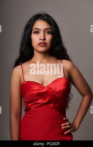 Studio Portrait Session von 17 Jahre alten Jugendlichen Mädchen mit einem roten Kleid auf einem grauen Hintergrund Stockfoto